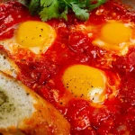 Chakchouka aux œufs dans une sauce tomate relevée, servie avec du pain et de la coriandre